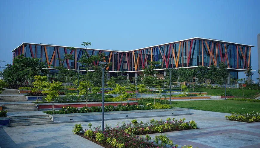 The BITSoM campus building in Mumbai, a low-rise glass structure with coloured vertical fins, seen across landscaped gardens