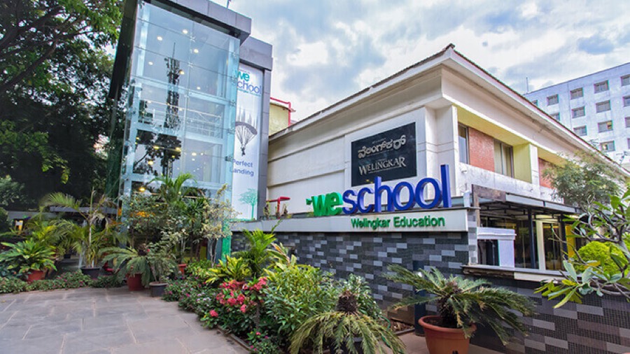 The WeSchool campus at Electronic City, Bengaluru — a low building with a glass lift shaft and the weschool Welingkar Education signage above the entrance