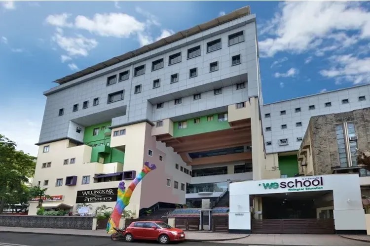 The WeSchool campus on Lakhamsi Napoo Road, Matunga, Mumbai — a multi-storey academic block behind the weschool gateway, with the institute's rainbow sculpture at the entrance